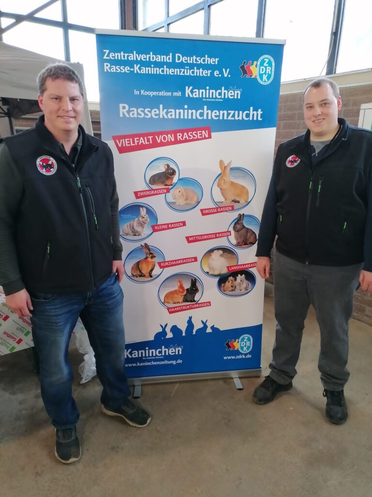 Die ZGM Marcel und Tobias Nöppert (v. l.) vor dem ZDRK-RollUp, das ihre beiden Satinkaninchen in Schwarz und Rot zeigt.